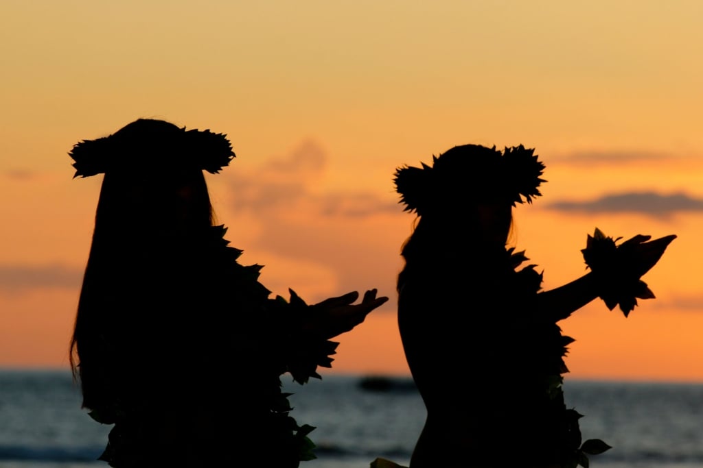 Hula dancers dancing at sunset near a beach.