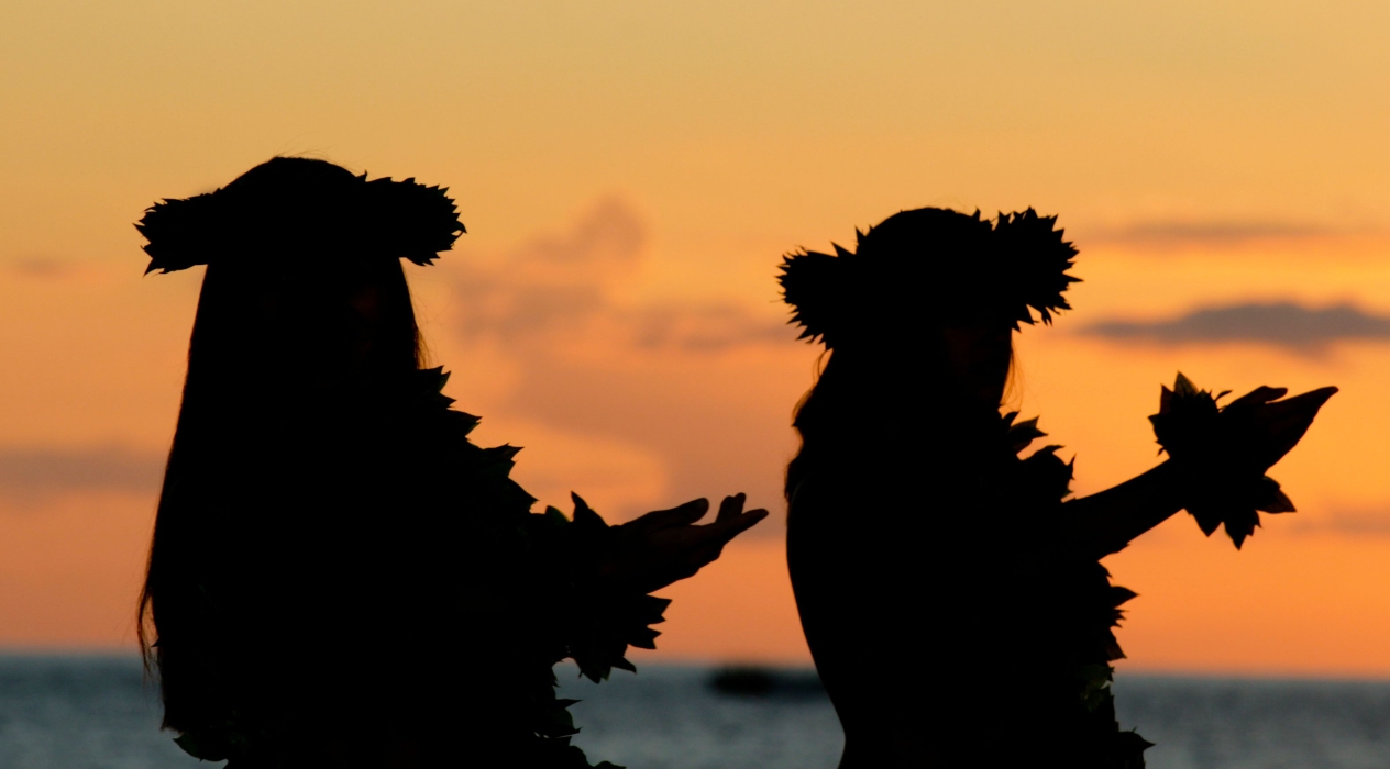 Hula dancers dancing at sunset near a beach.
