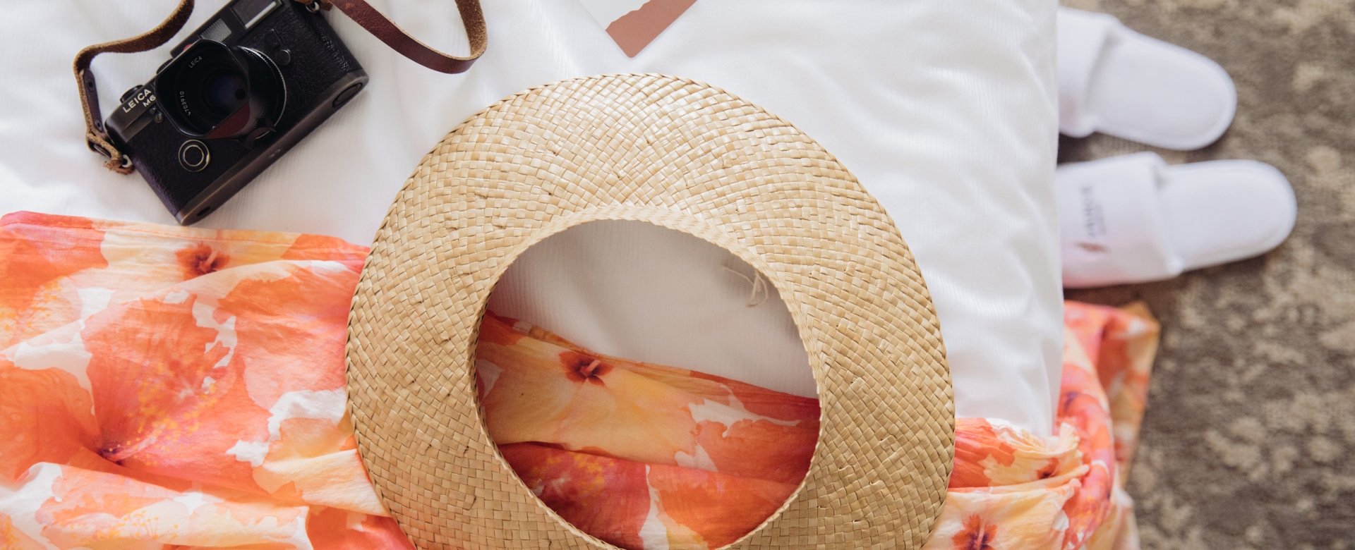 Camera on a bed with a Prince Waikiki room key and straw hat