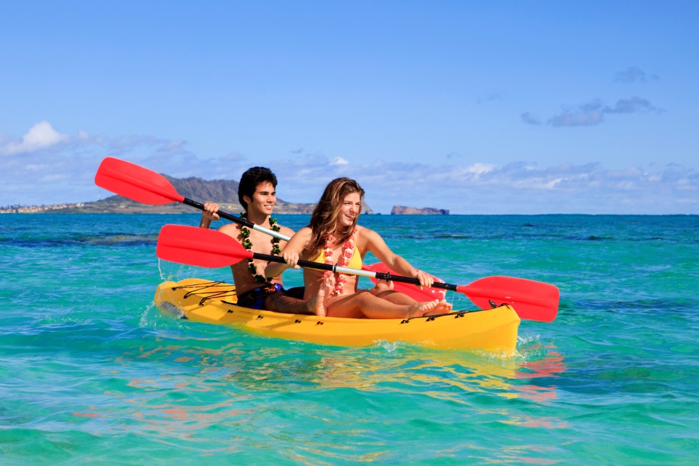 young couple with a kayak in hawaii paddling in the waters off the beach