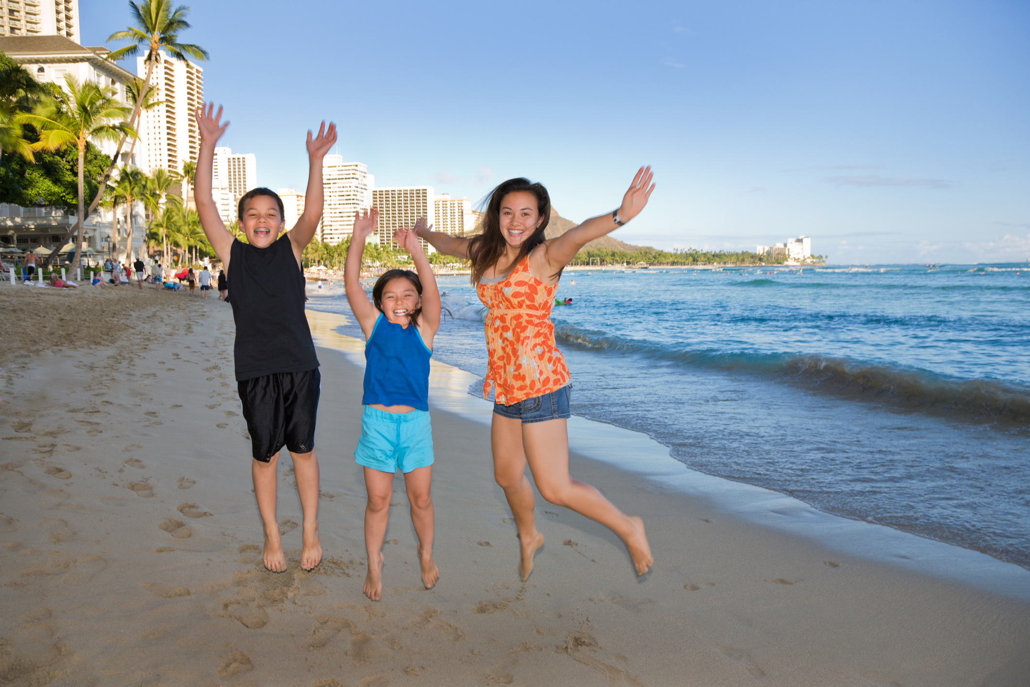 Three kids jump together on Waikiki Beach at sunset.