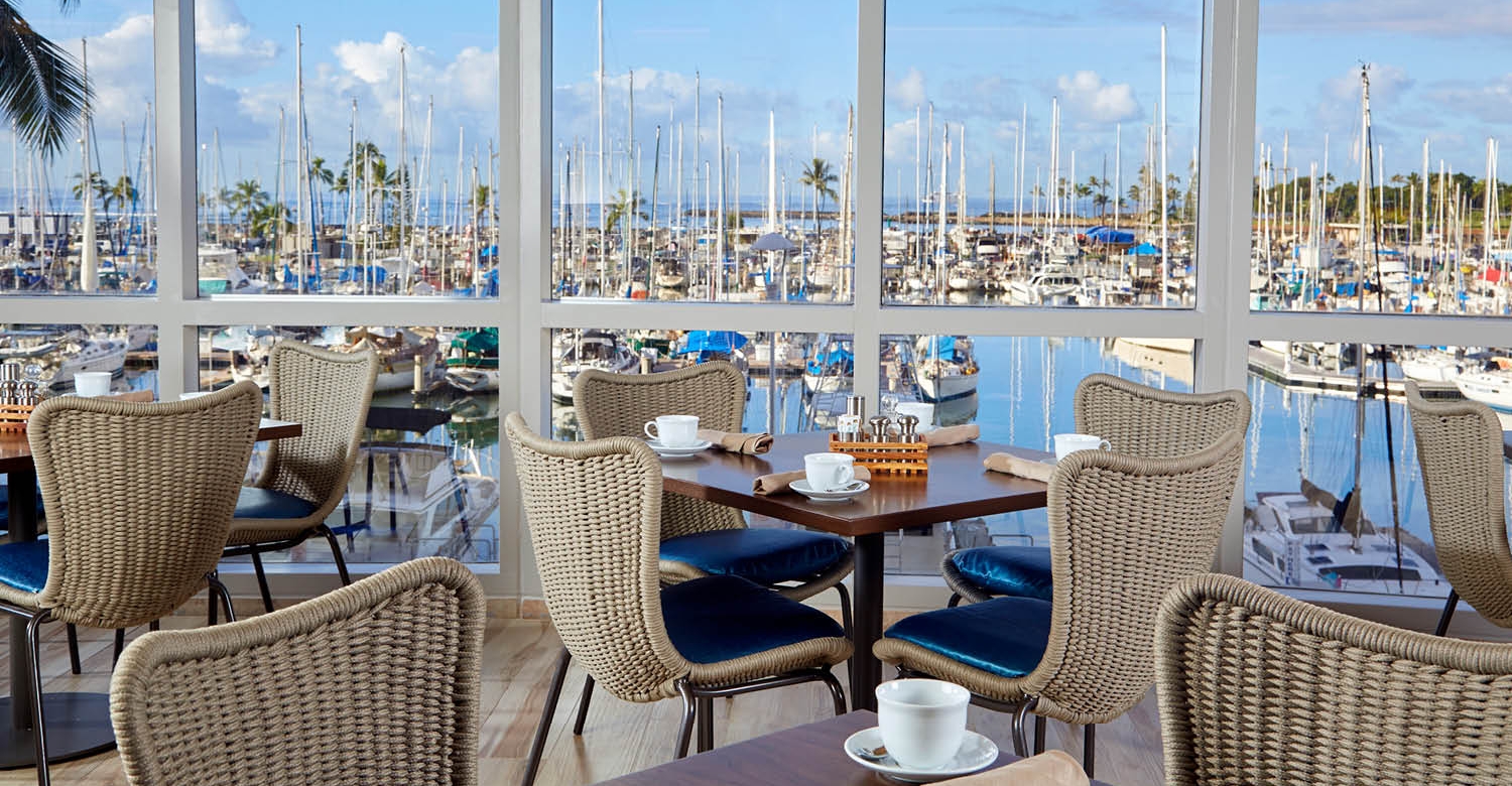 4 tables set for 4 with ocean views of the yacht harbor from the floor-to-ceiling windows at 100 Sails Restaurant & Bar in the Prince Waikiki Hotel.