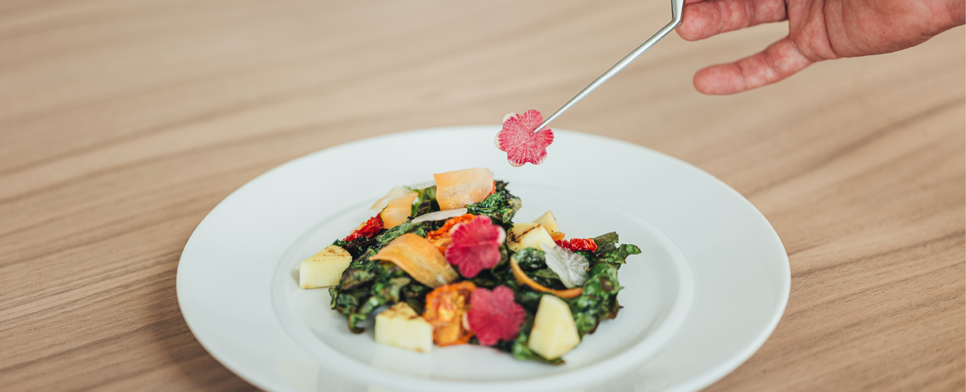 Chef's hand with a tweezer placing a sliced radish onto the Garden Melange Salad at 100 Sails Restaurant & Bar.