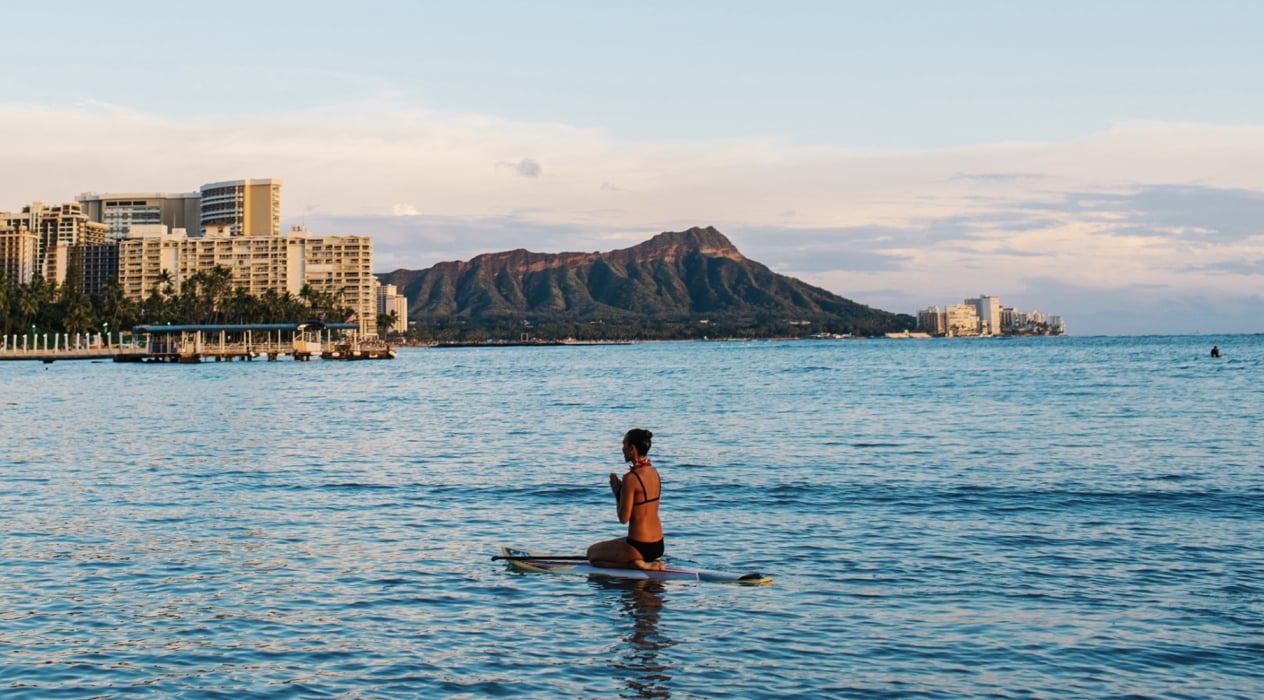 Woman mediating on surfboard at Waikiki Beach with views of Diamond Head.