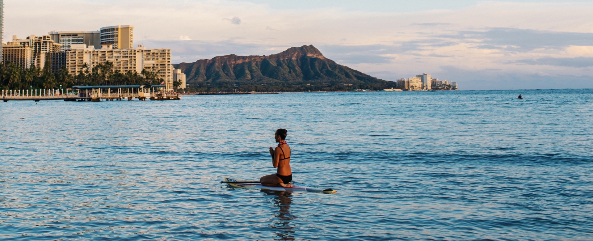 Woman mediating on surfboard at Waikiki Beach with views of Diamond Head.