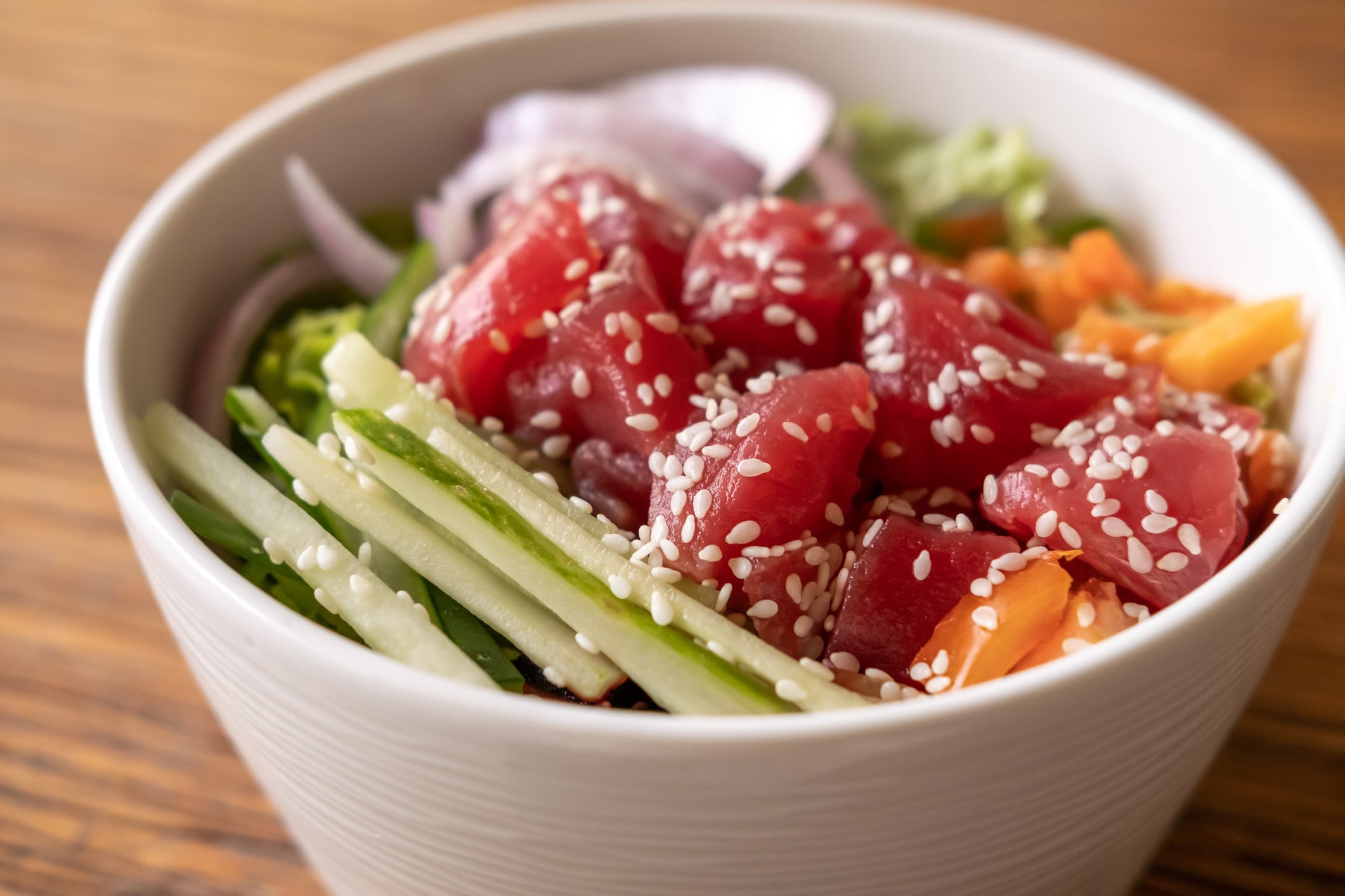 Healthy organic raw tuna Hawaiian poke bowl with cucumber, rice, carrots, onion served in bowl on wooden table.